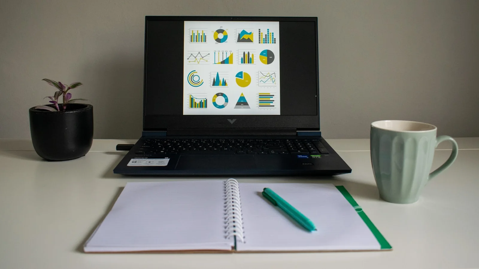 Notebook exibindo gráficos de análise ao lado de caderno e caneca